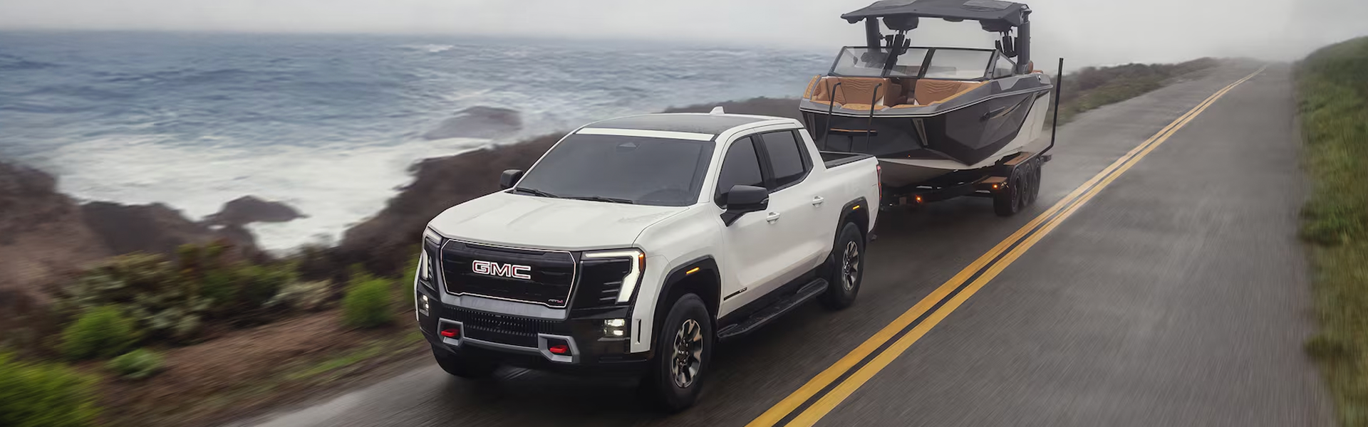 A white GMC Sierra EV towing a boat.